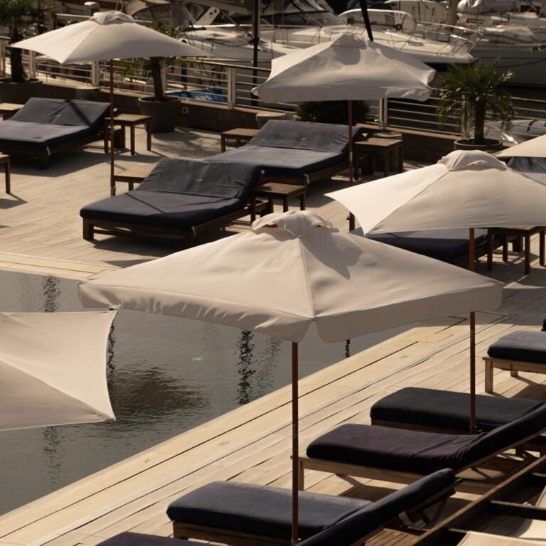 Panoramica della piscina del resort con file di ombrelloni bianchi e yacht ormeggiati sullo sfondo.