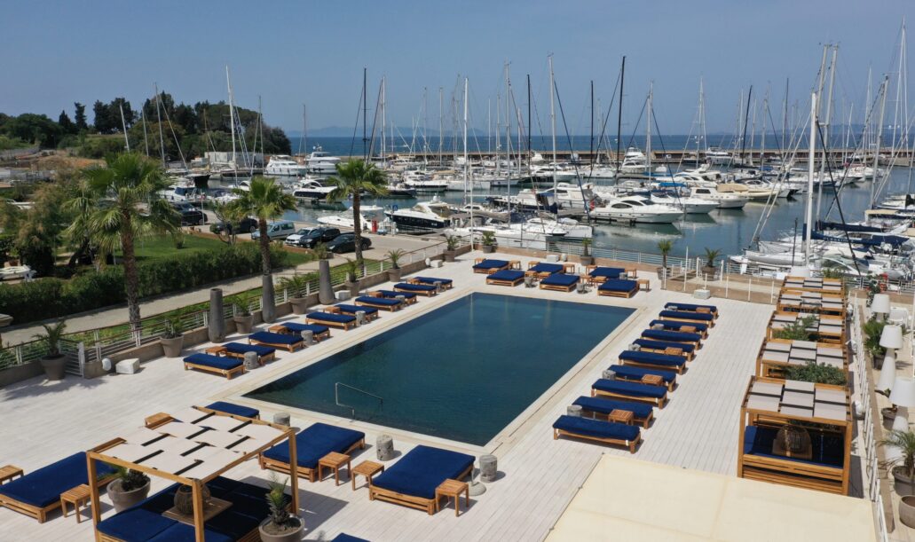 Panoramica della piscina del resort con file di ombrelloni bianchi e yacht ormeggiati sullo sfondo.