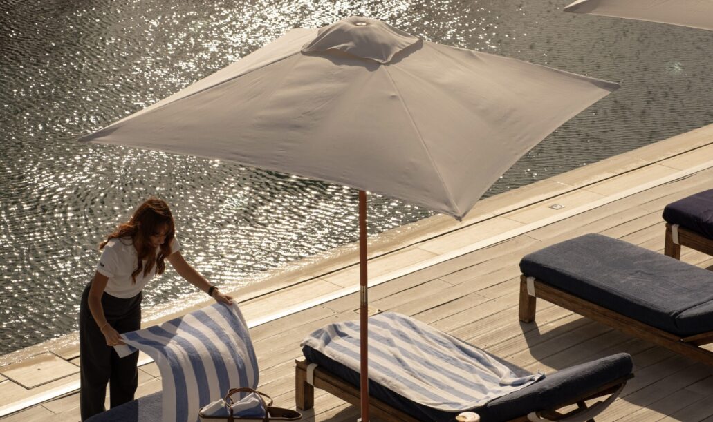 Personale del resort che prepara con cura i lettini a bordo piscina con teli rigati blu e bianchi.